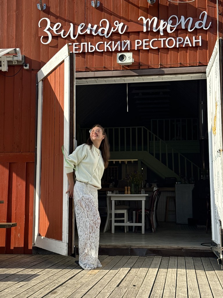 Улыбающаяся девушка стоит в дверях красного сельского ресторана на закате